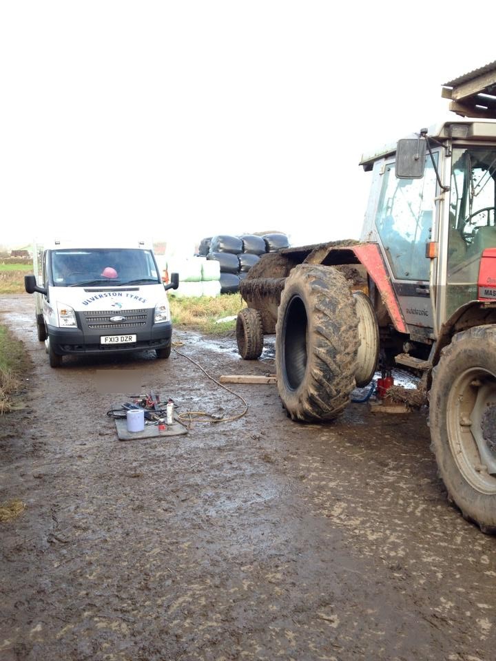 A red tractor with its rear wheel off in a farm gateway, the Ulverston Tyres van behind