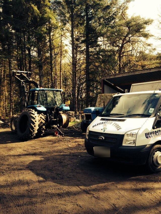 A blue tractor in a forest clearing with the Ulverston Tyres van
