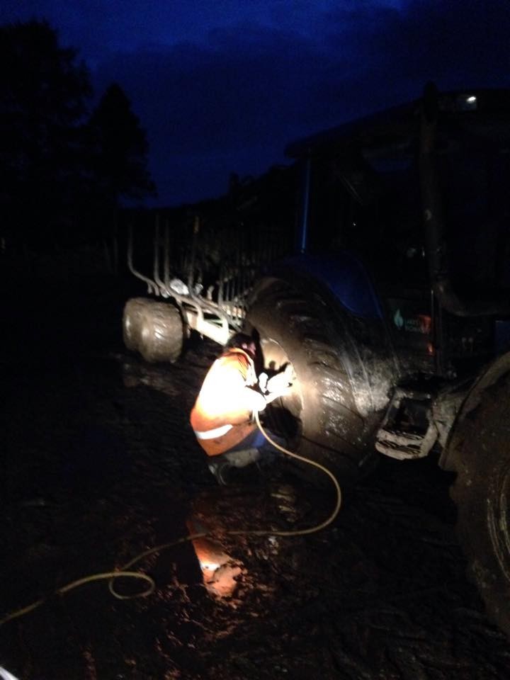 A night call-out: a fitter at a tractor wheel under a work light