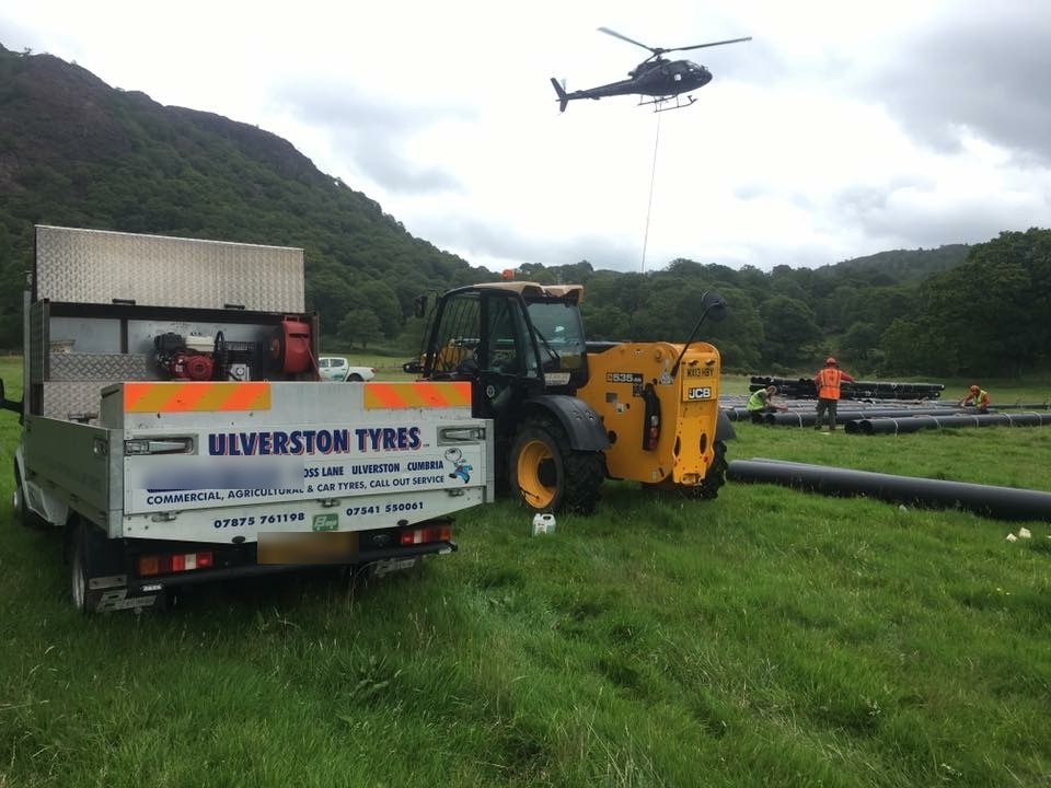 The Ulverston Tyres pickup on site in a valley field with a telehandler, a helicopter overhead